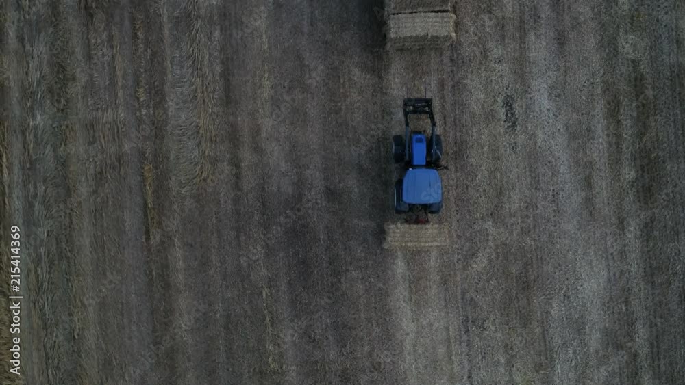 blue tractor moving hay stacks strawballs around aerial shot overview