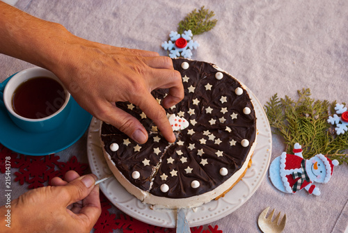 Woman handwith piece of christmas chocolate cake with holiday decoration:candle, garland, snowflakes and snowman. Food xmas background. photo