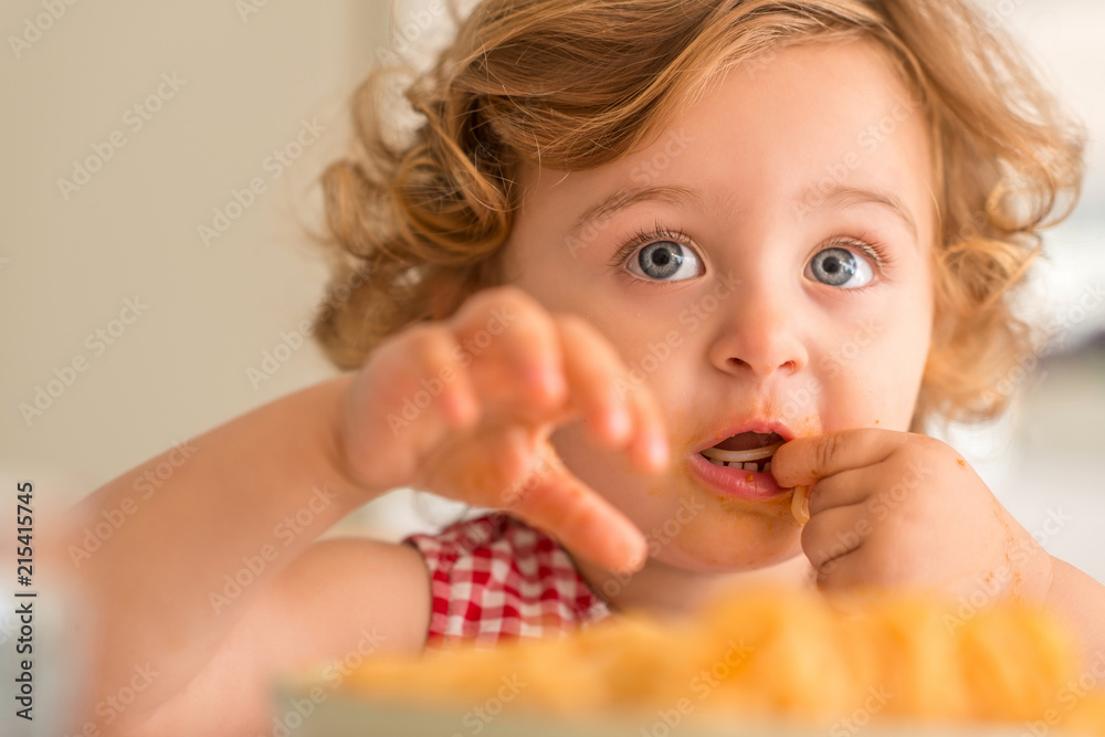 Close up of beautiful blond child eating spaghetti with hands at home. Close up of beautiful blond child eating spaghetti with hands at home.