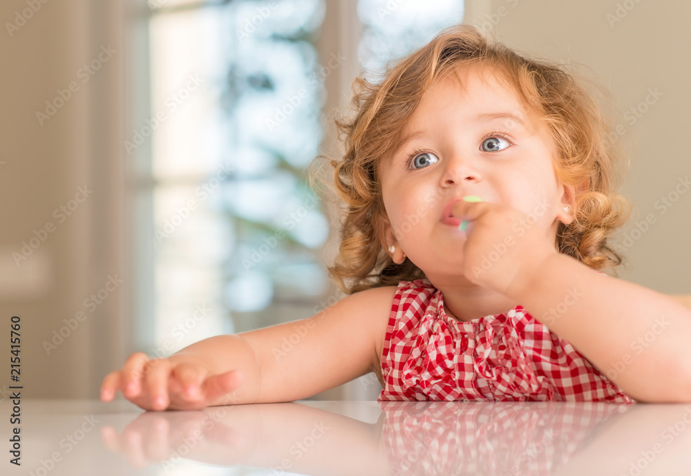 Fototapeta premium Beautiful blonde child with blue eyes eating candy at home.