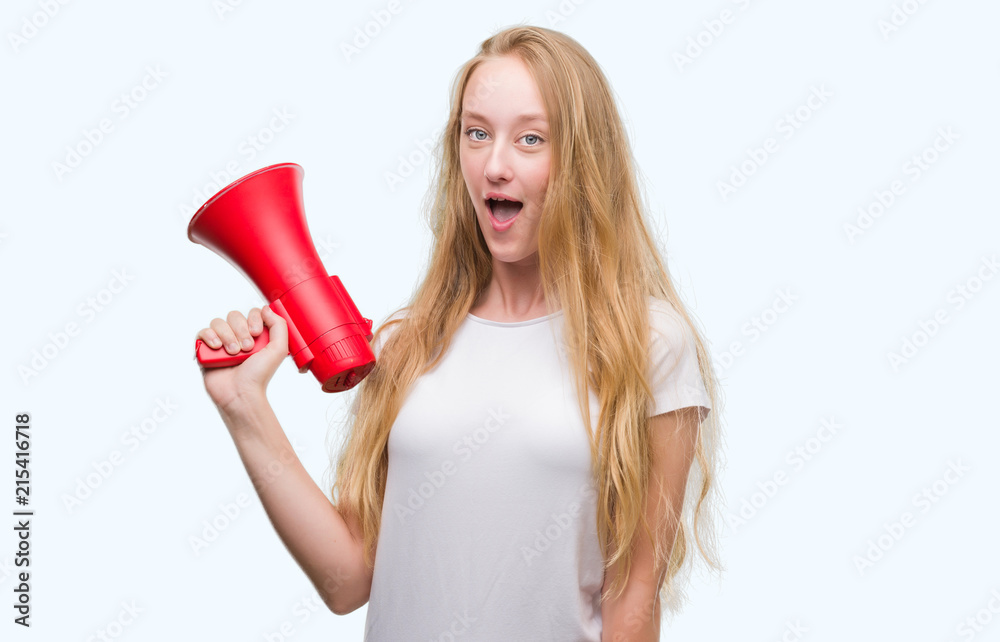 Blonde teenager woman holding megaphone scared in shock with a surprise face, afraid and excited with fear expression Blonde teenager woman holding megaphone scared in shock with a surprise face, afraid and excited with fear expression