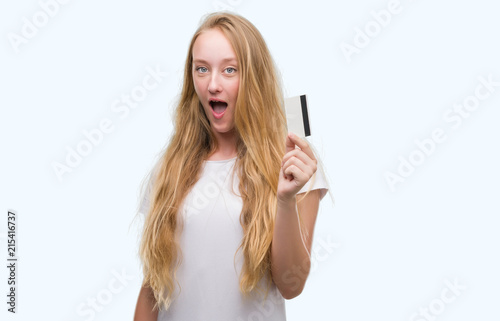 Blonde teenager woman holding credit card scared in shock with a surprise face, afraid and excited with fear expression