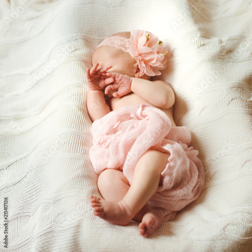 A sweet newborn baby in pink sleeps on a white knitted blanket, covering her sleeping face . Selective focus. Top view.