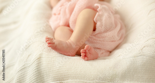 The legs of a newborn baby wrapped in a pink blanket lying on a white knitted blanket . Selective focus.