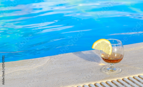 Blue pool water, a glass of flavored cognac with a slice of lemon at the water's edge