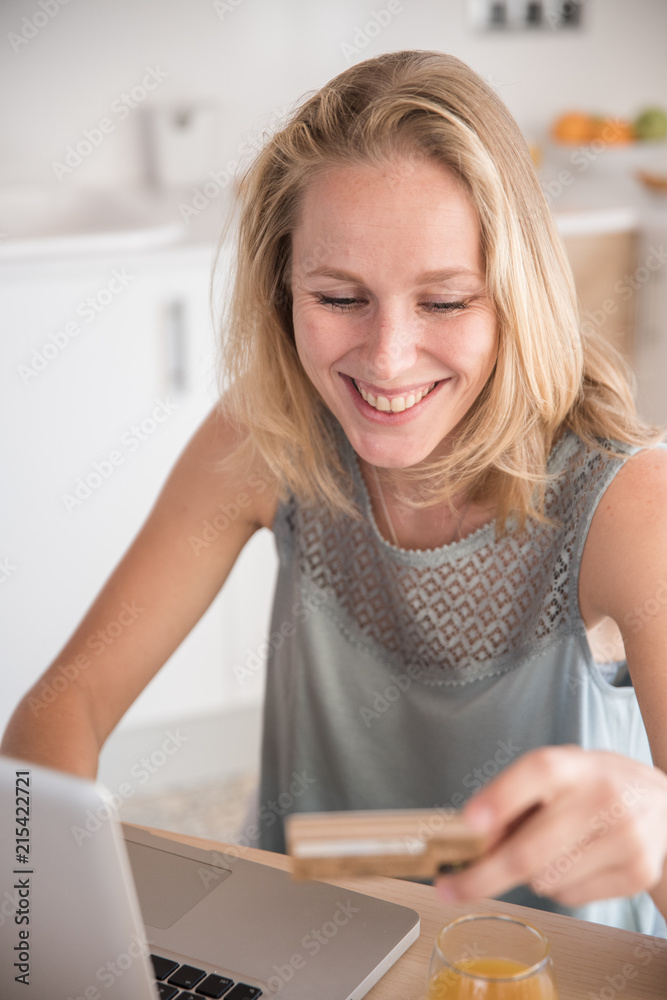 Woman smiling down at a credit card at her laptop Woman smiling down at a credit card at her laptop