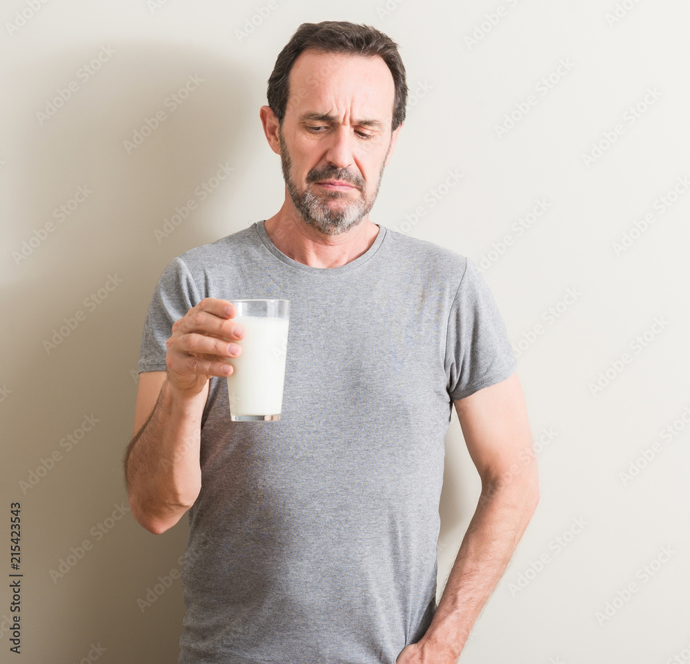 Senior man drinking a glass of milk with a confident expression on smart face thinking serious Senior man drinking a glass of milk with a confident expression on smart face thinking serious