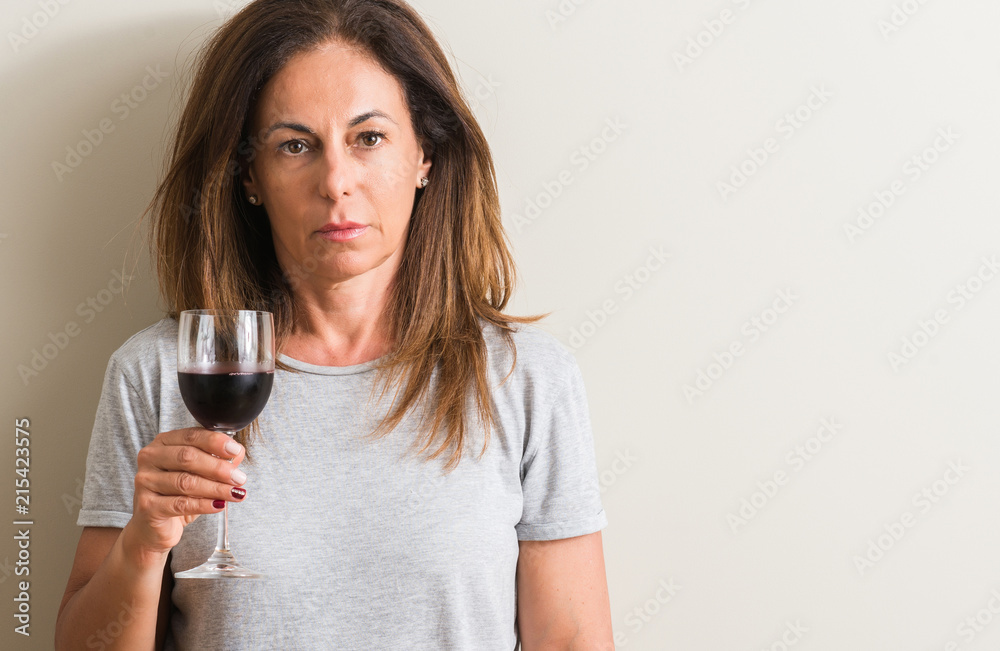 Middle age woman drinking red wine in a glass with a confident expression on smart face thinking serious Middle age woman drinking red wine in a glass with a confident expression on smart face thinking serious