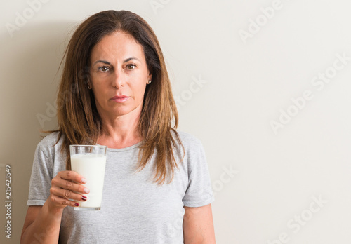 Middle age woman drinking a glass of fresh milk with a confident expression on smart face thinking serious