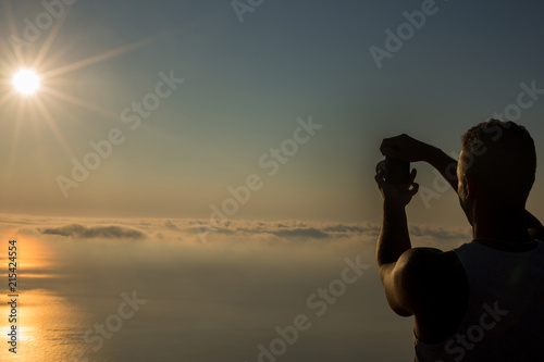 Handsome man taking photograph of a sunset above the clouds