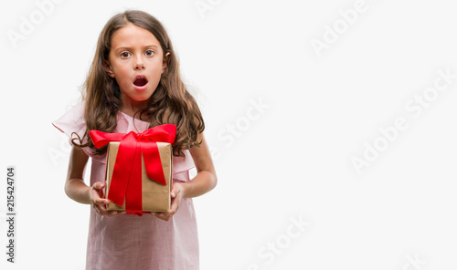 Brunette hispanic girl holding a gift scared in shock with a surprise face, afraid and excited with fear expression