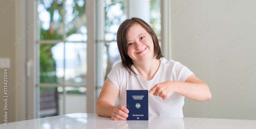 Down syndrome woman at home holding german passport very happy pointing with hand and finger Down syndrome woman at home holding german passport very happy pointing with hand and finger