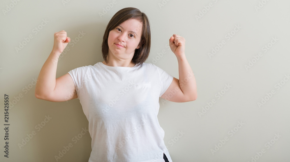 Down syndrome woman standing over wall showing arms muscles smiling proud. Fitness concept. Down syndrome woman standing over wall showing arms muscles smiling proud. Fitness concept.