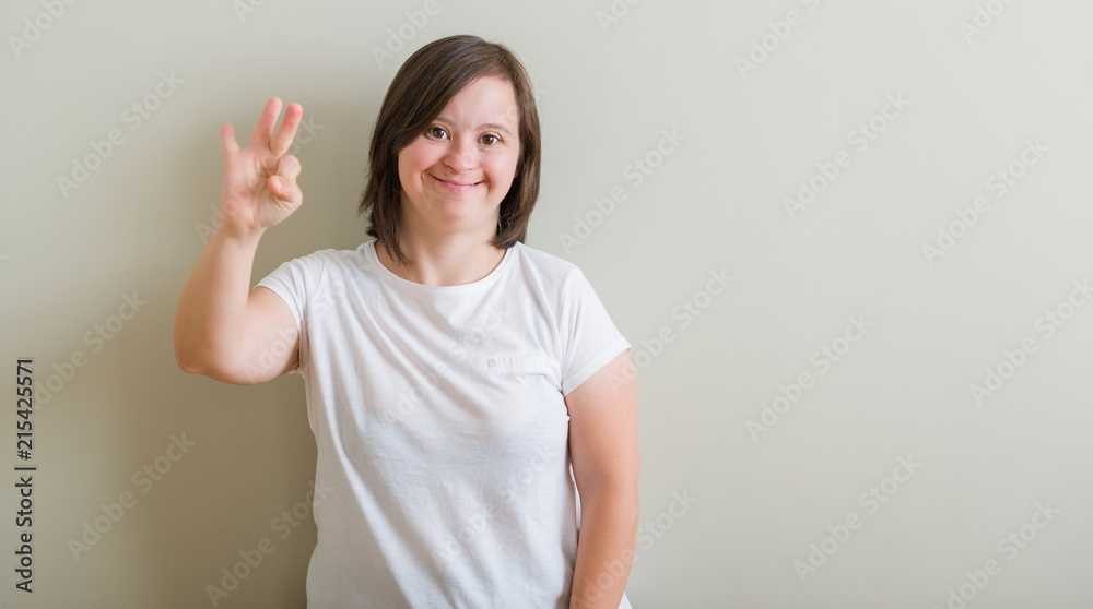Down syndrome woman standing over wall showing and pointing up with fingers number three while smiling confident and happy. Down syndrome woman standing over wall showing and pointing up with fingers number three while smiling confident and happy.