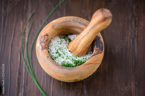 Dried Chives and Salt in a Mortar and Pestle to Make Herb Salt; Fresh Sprigs of Chives on Wooden Table in Background