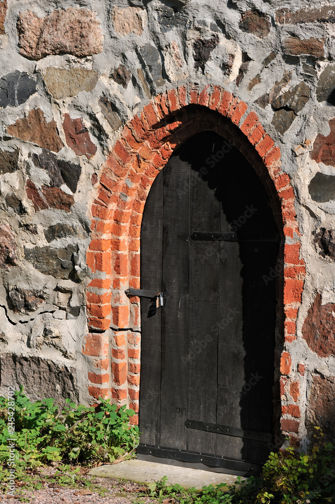 Old dark wooden door in medieval castle stone wall.