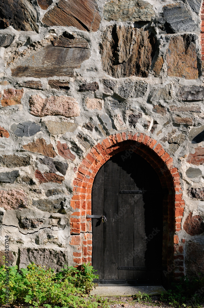 Old dark wooden door in medieval castle stone wall.