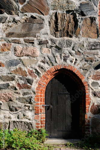 Old dark wooden door in medieval castle stone wall.