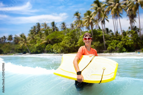 Child surfing on tropical beach. Surfer in ocean.