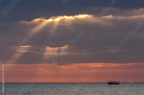 Sun rays breaking through clouds at sunset with traditional boat photo