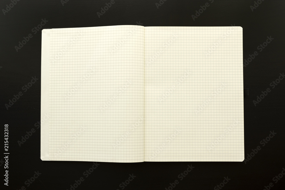 checkered sketchbook with pen on the side over black wooden table monochromatic flat lay composition