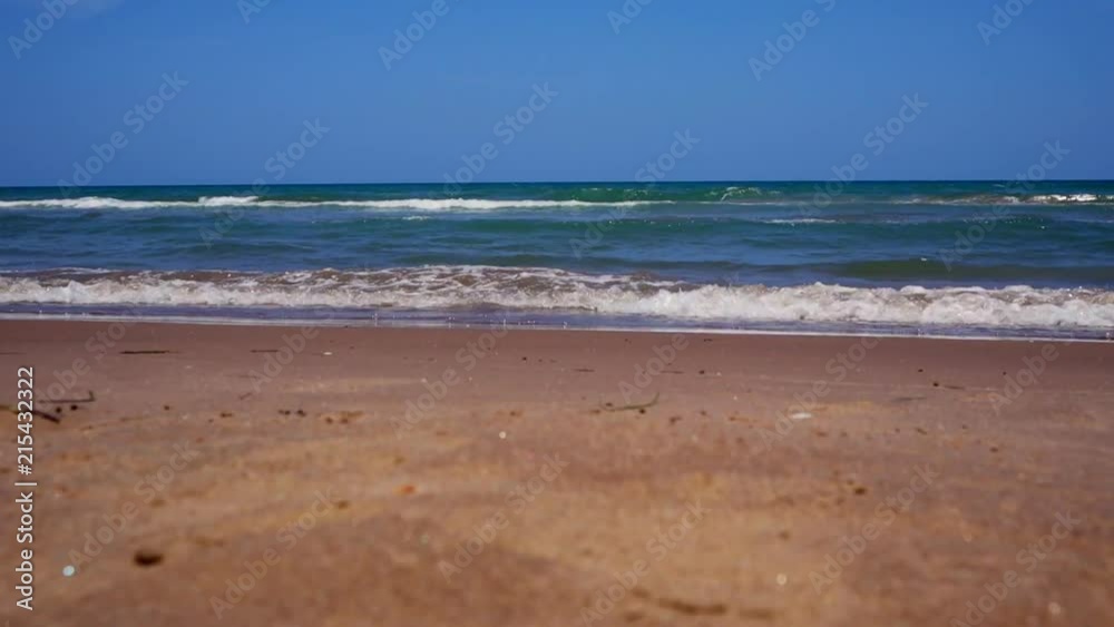 Low angle shot of waves crashing along beach shore with blue sky overhead. Low angle shot of waves crashing along beach shore with blue sky overhead.