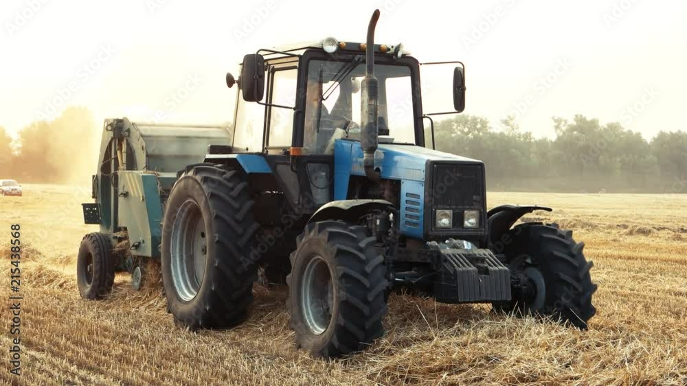 Working blue tractor in the field. Harvesting straw in bales from the field after harvest. Working blue tractor in the field. Harvesting straw in bales from the field after harvest.