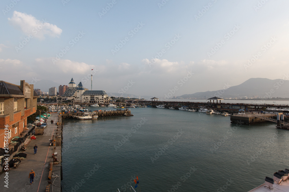 View from Fisherman's Wharf located along the coast of Tamsui District, New Taipei City Taiwan. Harbor with boats and sunset with calm water, ocean boats and buildings in the background.