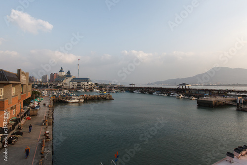 View from Fisherman's Wharf located along the coast of Tamsui District, New Taipei City Taiwan. Harbor with boats and sunset with calm water, ocean boats and buildings in the background.