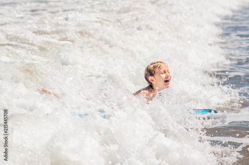 Happy baby boy - young surfer ride on surfboard with fun on sea waves. Active family lifestyle, kids outdoor water sport lessons and swimming activity in surf camp. Summer vacation with child photo
