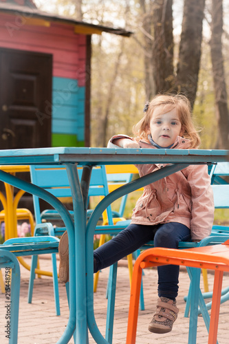 Fototapeta Naklejka Na Ścianę i Meble -  A child girl is sitting at a table outdoors against a background of a spring park