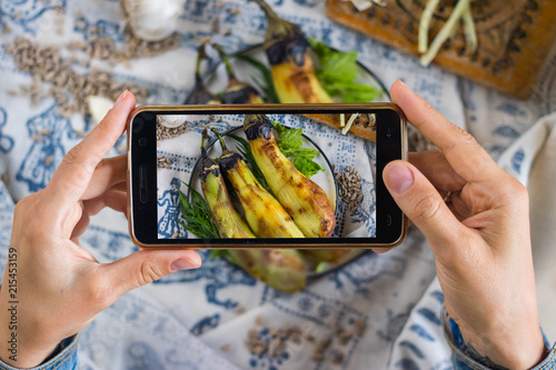 Woman hands takes smartphone food photo of roasted grilled vegetables lunch. Makes food photography for social networks or blogging with phone. Raw, vegan, vegetarian food