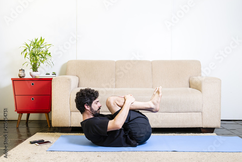 Beautiful caucasian bearded man in black clothes on blue yogamat doing wind removing pose photo