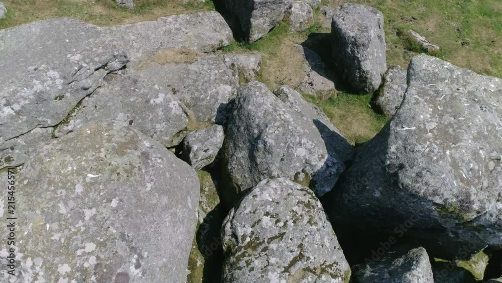 Closeup birdseye backward tracking aerial over a rocky tor environment with sheep hiding and taking shade within the boulders. Dartmoor, Devon, England Closeup birdseye backward tracking aerial over a rocky tor environment with sheep hiding and taking shade within the boulders. Dartmoor, Devon, England