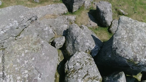 Closeup birdseye backward tracking aerial over a rocky tor environment with sheep hiding and taking shade within the boulders. Dartmoor, Devon, England photo