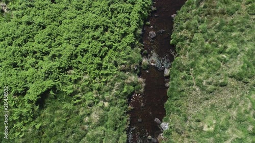Upward tracking aerial above a stunning dartmoor creek river, surrounded by green grassy moorland.Devon, England photo