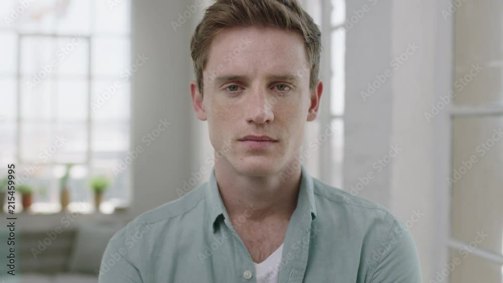 young handsome man portrait of red head guy looking serious pensive at camera in contemporary apartment background
