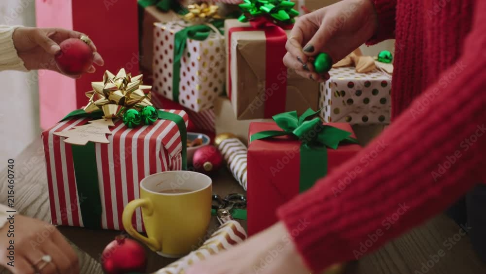 close up of two multi ethnic women wrapping christmas gifts using vibrant colorful paper young female friends wrap presents festive decorations celebration