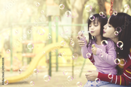 Mother and daughter having fun with soap bubbles at playground.