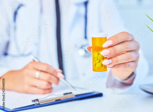 Female medicine doctor with jar of pills and write prescription to patient at worktable. Panacea and life save prescribing treatment legal drug store concept.