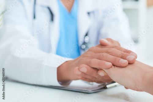 Hand of male doctor reassuring his female patient close-up. Medical ethics and trust concept.