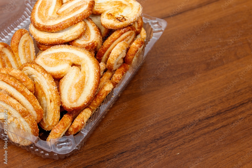 Palmier biscuits - french cookies made of puff pastry (also called palm leaves, elephant ears or french hearts) packed in plastic box on wooden table