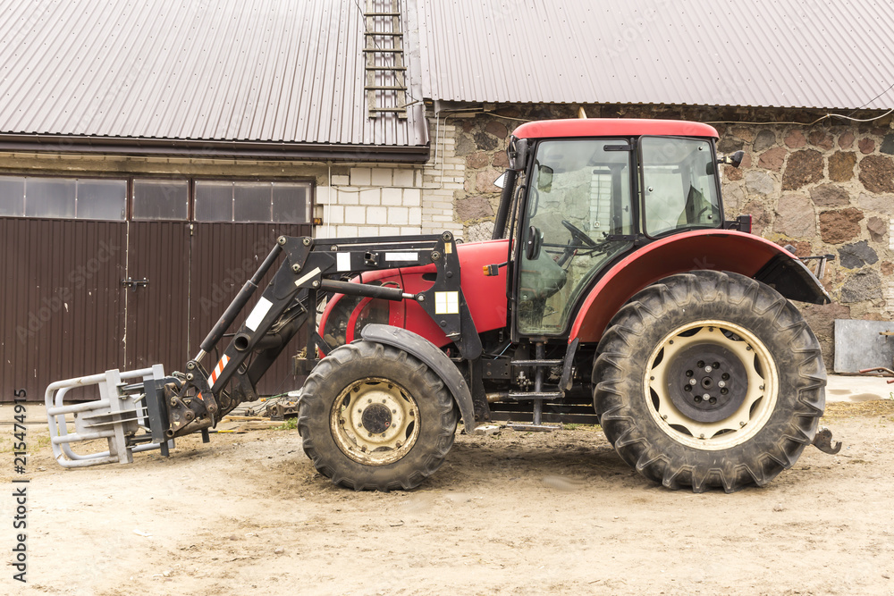 Tractor with hydraulic lift for carrying bales of hay and silage. Picture of the side of the agricultural machine. The equipment for a dairy farm. Tractor with hydraulic lift for carrying bales of hay and silage. Picture of the side of the agricultural machine. The equipment for a dairy farm.