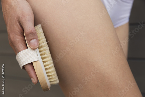 Woman's arm holding dry brush to top of her leg. Cellulite treatment, dry brushing