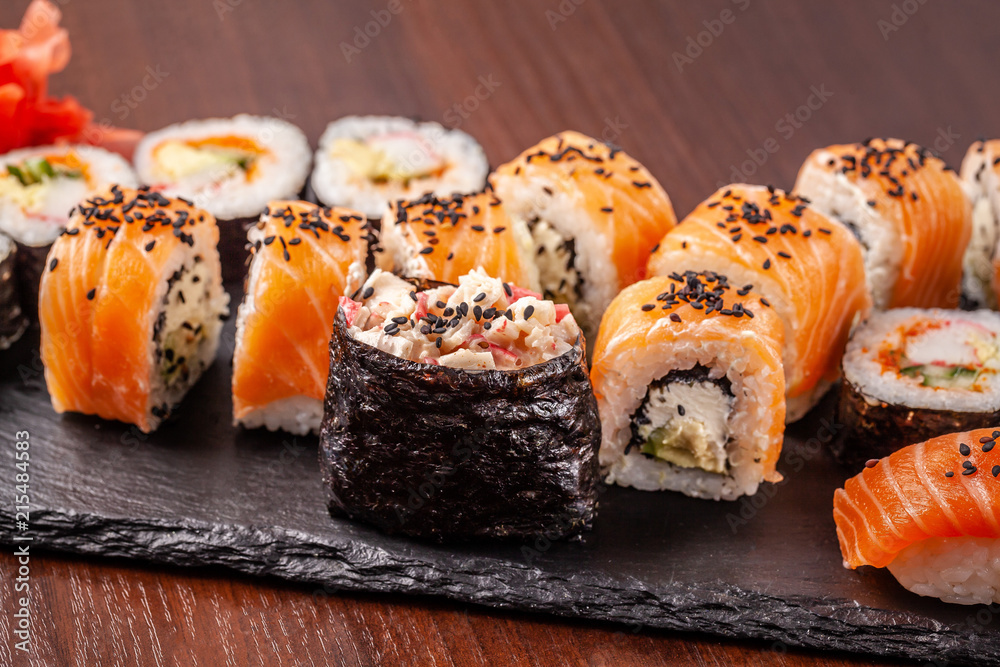 Asian traditional cuisine. A large set of rolls and sushi on a black slate stone, on a wooden table in a restaurant, with soy sauce and Chinese chopsticks. Asian traditional cuisine. A large set of rolls and sushi on a black slate stone, on a wooden table in a restaurant, with soy sauce and Chinese chopsticks.