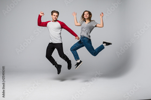 Full length portrait of a cheerful young couple jumping and running over white wall