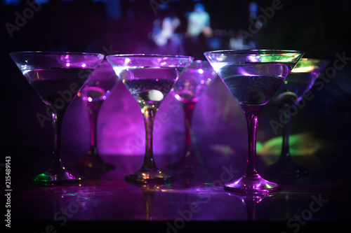 Several glasses of famous cocktail Martini, shot at a bar with dark toned foggy background and disco lights. Club drink concept