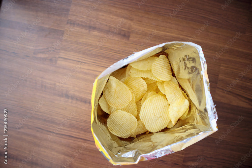 Potato chips in open snack bag close up on table floor