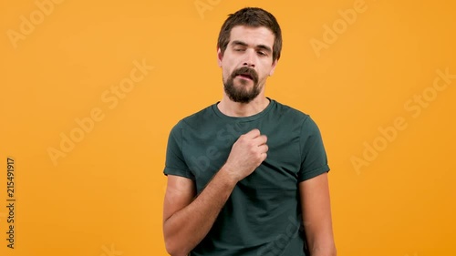 Bored man wearing a casual green t-shirt and chewing gum on yellow orange background