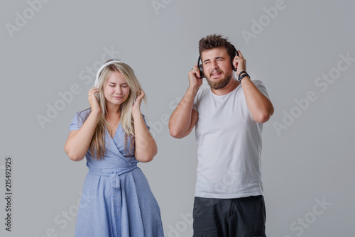 Young cheerful couple listening to loud music in wireless headphones. A girl waving long hair and dancing, holding hands near the ears